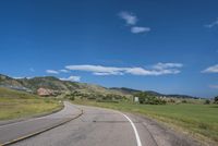 an empty road near mountains with hills in the background on a clear, sunny day