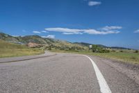 an empty road near mountains with hills in the background on a clear, sunny day