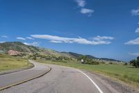 an empty road near mountains with hills in the background on a clear, sunny day
