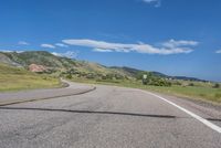 an empty road near mountains with hills in the background on a clear, sunny day