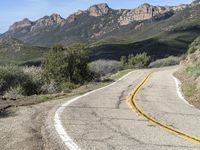 the curve has been painted white on the side of the mountain road, with mountains in the distance