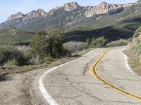 the curve has been painted white on the side of the mountain road, with mountains in the distance