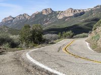 the curve has been painted white on the side of the mountain road, with mountains in the distance