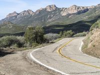 the curve has been painted white on the side of the mountain road, with mountains in the distance