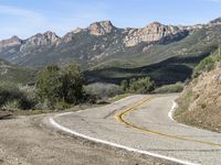 the curve has been painted white on the side of the mountain road, with mountains in the distance