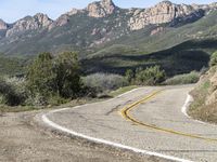 the curve has been painted white on the side of the mountain road, with mountains in the distance