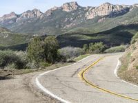 the curve has been painted white on the side of the mountain road, with mountains in the distance