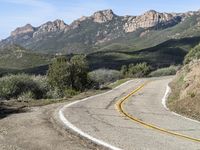 the curve has been painted white on the side of the mountain road, with mountains in the distance