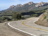 the curve has been painted white on the side of the mountain road, with mountains in the distance