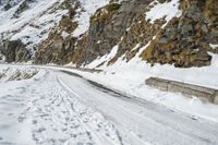 a mountain scene with a very narrow mountain road near the snow covered mountains and a rock face