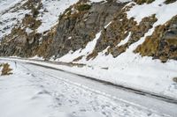 a mountain scene with a very narrow mountain road near the snow covered mountains and a rock face