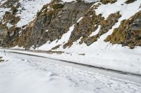 a mountain scene with a very narrow mountain road near the snow covered mountains and a rock face