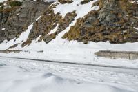 a mountain scene with a very narrow mountain road near the snow covered mountains and a rock face