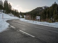 a long mountain road with a sign in the middle of it near a forest and mountains