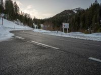 a long mountain road with a sign in the middle of it near a forest and mountains