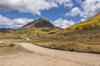 an empty road leading through a mountain meadow with a dirt road, mountains and a blue sky in the background