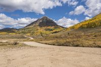 an empty road leading through a mountain meadow with a dirt road, mountains and a blue sky in the background