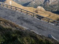 a train is riding on a winding road by the side of a mountain pass, as seen from the hill below