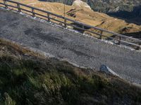 a train is riding on a winding road by the side of a mountain pass, as seen from the hill below