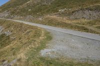 a dirt road that passes between a steep mountain and grassy area on the far side of the road