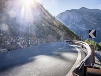 a car drives along an empty mountain side road in the daytime sunshine and lens flares out