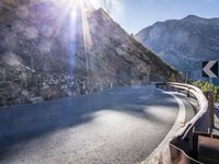a car drives along an empty mountain side road in the daytime sunshine and lens flares out