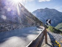 a car drives along an empty mountain side road in the daytime sunshine and lens flares out