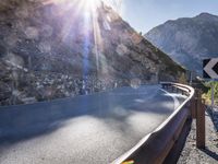 a car drives along an empty mountain side road in the daytime sunshine and lens flares out