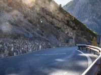 a car drives along an empty mountain side road in the daytime sunshine and lens flares out