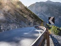 a car drives along an empty mountain side road in the daytime sunshine and lens flares out