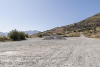 a couple of cars are parked on top of gravel road near mountains and hills with trees in them