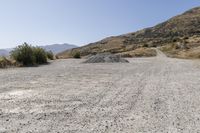 a couple of cars are parked on top of gravel road near mountains and hills with trees in them