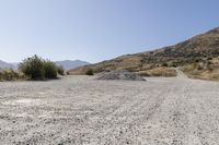 a couple of cars are parked on top of gravel road near mountains and hills with trees in them