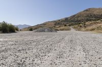 a couple of cars are parked on top of gravel road near mountains and hills with trees in them