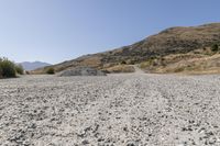 a couple of cars are parked on top of gravel road near mountains and hills with trees in them