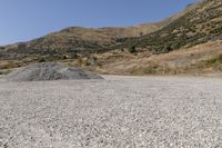 a couple of cars are parked on top of gravel road near mountains and hills with trees in them