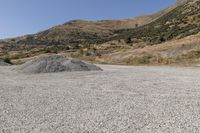 a couple of cars are parked on top of gravel road near mountains and hills with trees in them