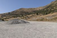 a couple of cars are parked on top of gravel road near mountains and hills with trees in them