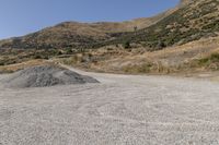 a couple of cars are parked on top of gravel road near mountains and hills with trees in them