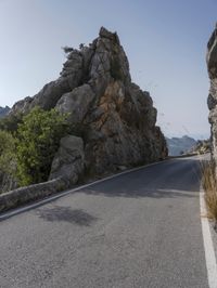 the road in the mountains is lined by rocks and boulders with a sky background and birds flying overhead