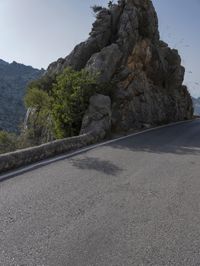 the road in the mountains is lined by rocks and boulders with a sky background and birds flying overhead