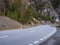 a curve road with a mountain in the distance and trees and mountain peaks in the background