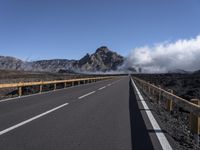 an empty roadway and clouds over mountains, during the day on a sunny day with clear skies