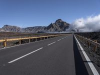 an empty roadway and clouds over mountains, during the day on a sunny day with clear skies