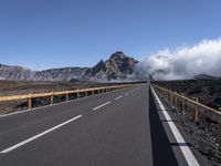 an empty roadway and clouds over mountains, during the day on a sunny day with clear skies