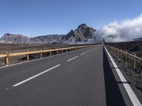 an empty roadway and clouds over mountains, during the day on a sunny day with clear skies