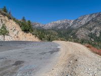 a dirt and gravel road with mountains in the background and trees on both sides of the road