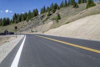 a mountain landscape with a long curving road and parked cars on it's side