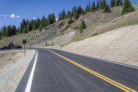 a mountain landscape with a long curving road and parked cars on it's side