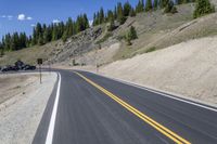 a mountain landscape with a long curving road and parked cars on it's side